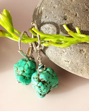 Load image into Gallery viewer, A pair of turquoise nuggets and Malachite are hand wire wrapped and combined with sterling silver findings styled with green stems and smooth gray stones on a light beige surface.