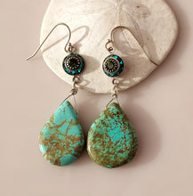 Load image into Gallery viewer, A pair of dangle earrings with teardrop shaped turquoise drops hand wire-wrapped to blue and green Swarovski Crystal link. Sterling Silver findings. are displayed on a white seashell against a soft pink background.