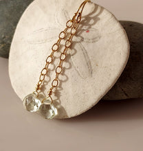 Load image into Gallery viewer, A pair of drop earrings with 14 karat gold-filled wire and findings with a dangling faceted green amethyst gemstone displayed on a white sand dollar shell.