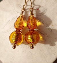 Load image into Gallery viewer, A pair of dangling earrings with faceted amber-gold Swarovski Crystal beads and textured gold Murano glass round beads, using 14 karat gold-filled findings hanging against a light textured background.