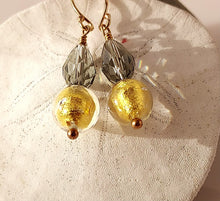 Load image into Gallery viewer, A pair of handmade dangle earrings with gold Murano glass beads and silvery Swarovski Crystal beads,14 karat Gold-filled fishhook wires, on a light pink background.