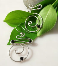 Load image into Gallery viewer, A pair of handmade sterling silver spiral wire hoop earrings with hand wire-wrapped black onyx beads, displayed on vibrant green leaves against a clean white background.