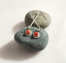 Load image into Gallery viewer, A pair of Sterling Silver dangle earrings with round Carnelian stones in a scalloped floral setting, displayed on smooth dark gray stones against a light neutral background.