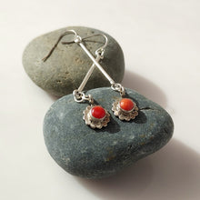 Load image into Gallery viewer, A pair of Sterling Silver dangle earrings with round Carnelian stones in a scalloped floral setting, displayed on smooth dark gray stones against a light neutral background.