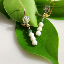 Load image into Gallery viewer, A pair of gold dangle earrings with light blue Swaroski Crystal clusters, Chyrsolite and white coral beads, displayed on a large green leaf against a white background.