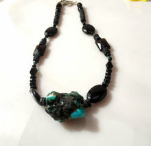 Load image into Gallery viewer, A beaded necklace featuring black Onyx faceted beads, black Onyx oval beads, and a prominent natural turquoise and black stone pendant, displayed on a light off-white surface.