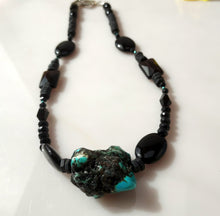 Load image into Gallery viewer, A beaded necklace featuring black Onyx faceted beads, black Onyx oval beads, and a prominent natural turquoise and black stone pendant, displayed on a light off-white surface.
