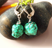 Load image into Gallery viewer, A pair of turquoise nuggets and Malachite are hand wire wrapped and combined with sterling silver findings styled with green stems and smooth gray stones on a light beige surface.
