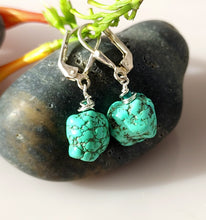 Load image into Gallery viewer, A pair of turquoise nuggets and Malachite are hand wire wrapped and combined with sterling silver findings styled with green stems and smooth gray stones on a light beige surface.
