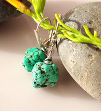 Load image into Gallery viewer, A pair of turquoise nuggets and Malachite are hand wire wrapped and combined with sterling silver findings styled with green stems and smooth gray stones on a light beige surface.
