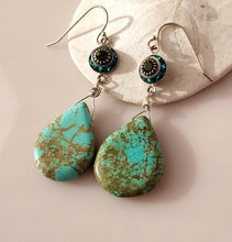 Load image into Gallery viewer, A pair of dangle earrings with teardrop shaped turquoise drops hand  wire-wrapped to blue and green Swarovski Crystal link. Sterling Silver findings. are displayed on a white seashell against a soft pink background.
