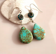 Load image into Gallery viewer, A pair of dangle earrings with teardrop shaped turquoise drops hand  wire-wrapped to blue and green Swarovski Crystal link. Sterling Silver findings. are displayed on a white seashell against a soft pink background.

