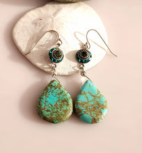 Load image into Gallery viewer, A pair of dangle earrings with teardrop shaped turquoise drops hand  wire-wrapped to blue and green Swarovski Crystal link. Sterling Silver findings. are displayed on a white seashell against a soft pink background.
