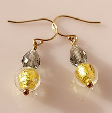 Load image into Gallery viewer, A pair of handmade dangle earrings with gold Murano glass beads and silvery Swarovski Crystal beads,14 karat Gold-filled fishhook wires, on a light pink background.
