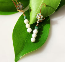 Load image into Gallery viewer, A pair of gold dangle earrings with light blue Swaroski Crystal clusters, Chyrsolite and white coral beads, displayed on a large green leaf against a white background.
