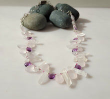 Load image into Gallery viewer, A beaded necklace made of clear quartz crystal points and pale pink rose quartz beads, accented with small purple amethyst beads, displayed on a white surface with dark gray decorative stones.
