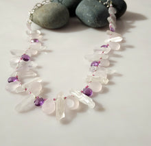 Load image into Gallery viewer, A beaded necklace made of clear quartz crystal points and pale pink rose quartz beads, accented with small purple amethyst beads, displayed on a white surface with dark gray decorative stones.
