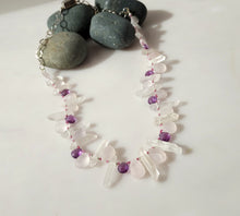 Load image into Gallery viewer, A beaded necklace made of clear quartz crystal points and pale pink rose quartz beads, accented with small purple amethyst beads, displayed on a white surface with dark gray decorative stones.
