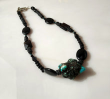 Load image into Gallery viewer, A beaded necklace featuring black Onyx faceted beads, black Onyx oval beads, and a prominent natural turquoise and black stone pendant, displayed on a light off-white surface.

