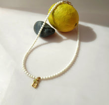 Load image into Gallery viewer, A beaded necklace made of small white jade beads with a 14 karat gold-filled padlock pendant featuring a heart and and a small green gemstone charm, and a lobster claw clasp.
